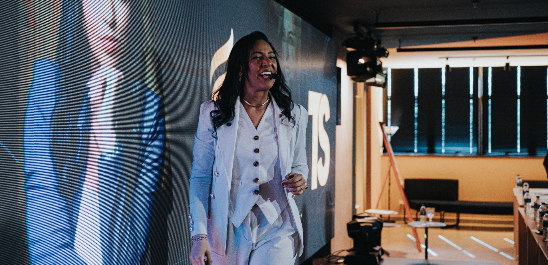 Débora Santos palestrando em auditório do Grupo TS, diante do painel de LED